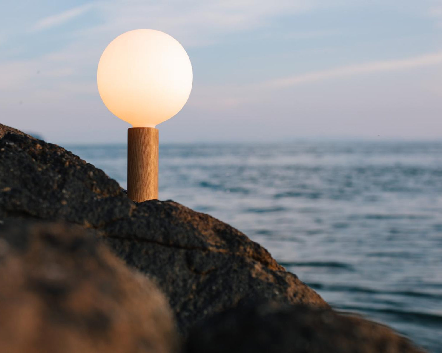 Knuckle Table Lamp in Oak + Sphere IV outside on a mountain in front of a body of water