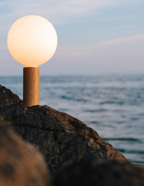 Knuckle Table Lamp in Oak + Sphere IV outside on a mountain in front of a body of water
