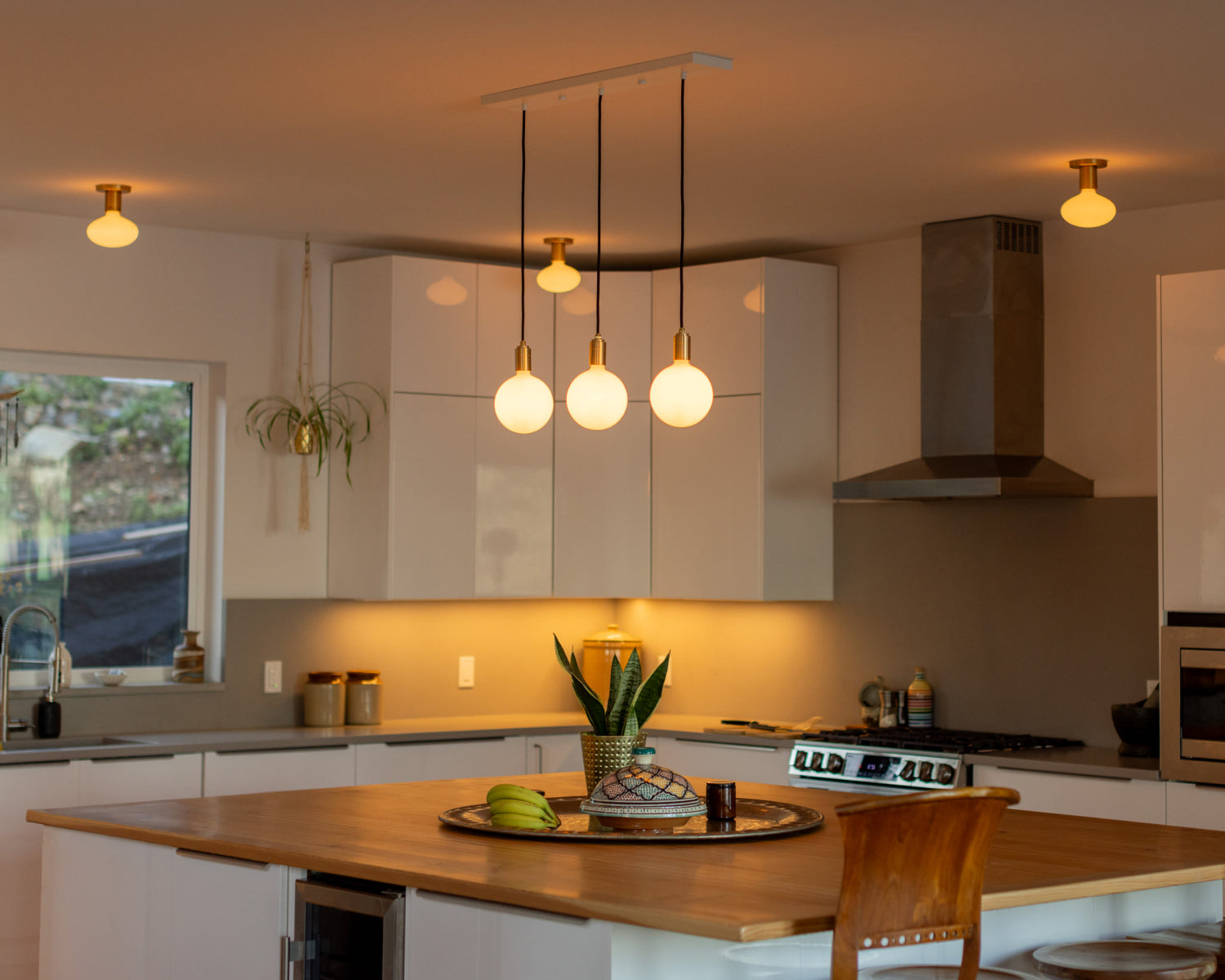 Linear pendant with Sphere IV bulbs hanging above kitchen island with Lochan Wall Lights